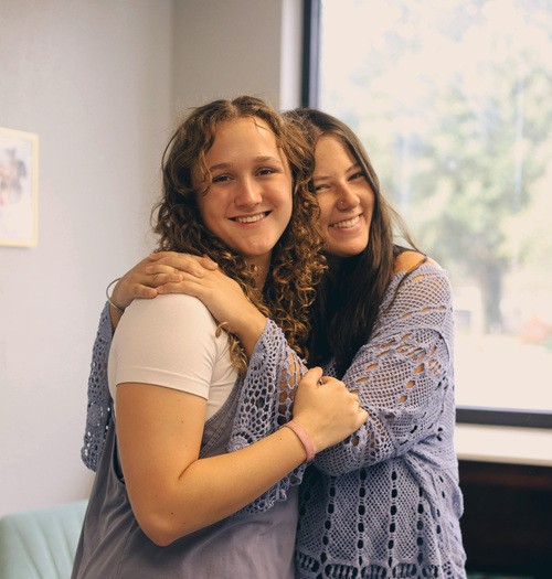 Two young women hugging and smiling at camera.