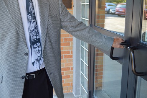 A man in a suit coat and Elvis tie opens the door on a Sunday morning at NABC